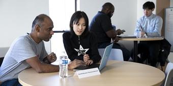 Two students work on a laptop at a round table