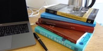 Stack of books sitting on a desk next to a laptop